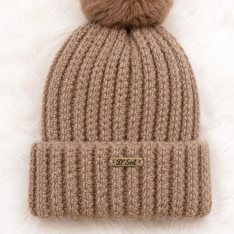 Close do ponto de um gorro de crochê caramelo, com a etiqueta de metal D' Sol costurada